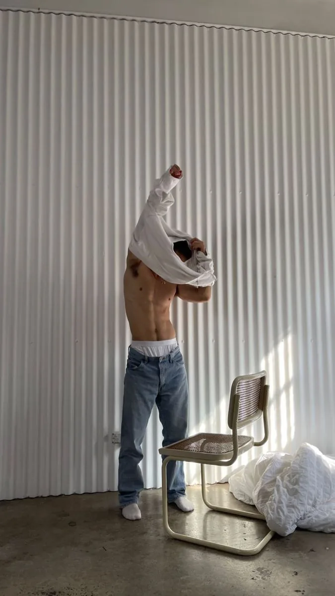 Man pulling a white T-shirt over his head, Majella waistband visible